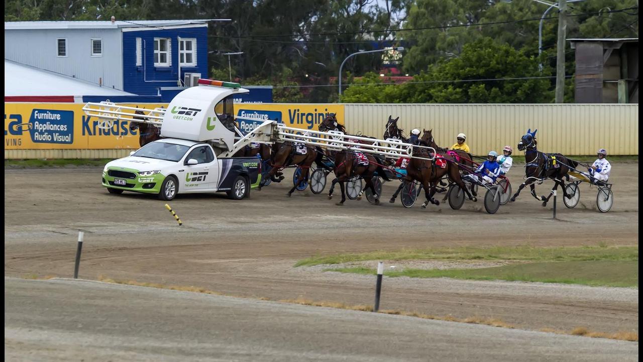Harness horses lined up behind the mobile starting gate car at the start of a race